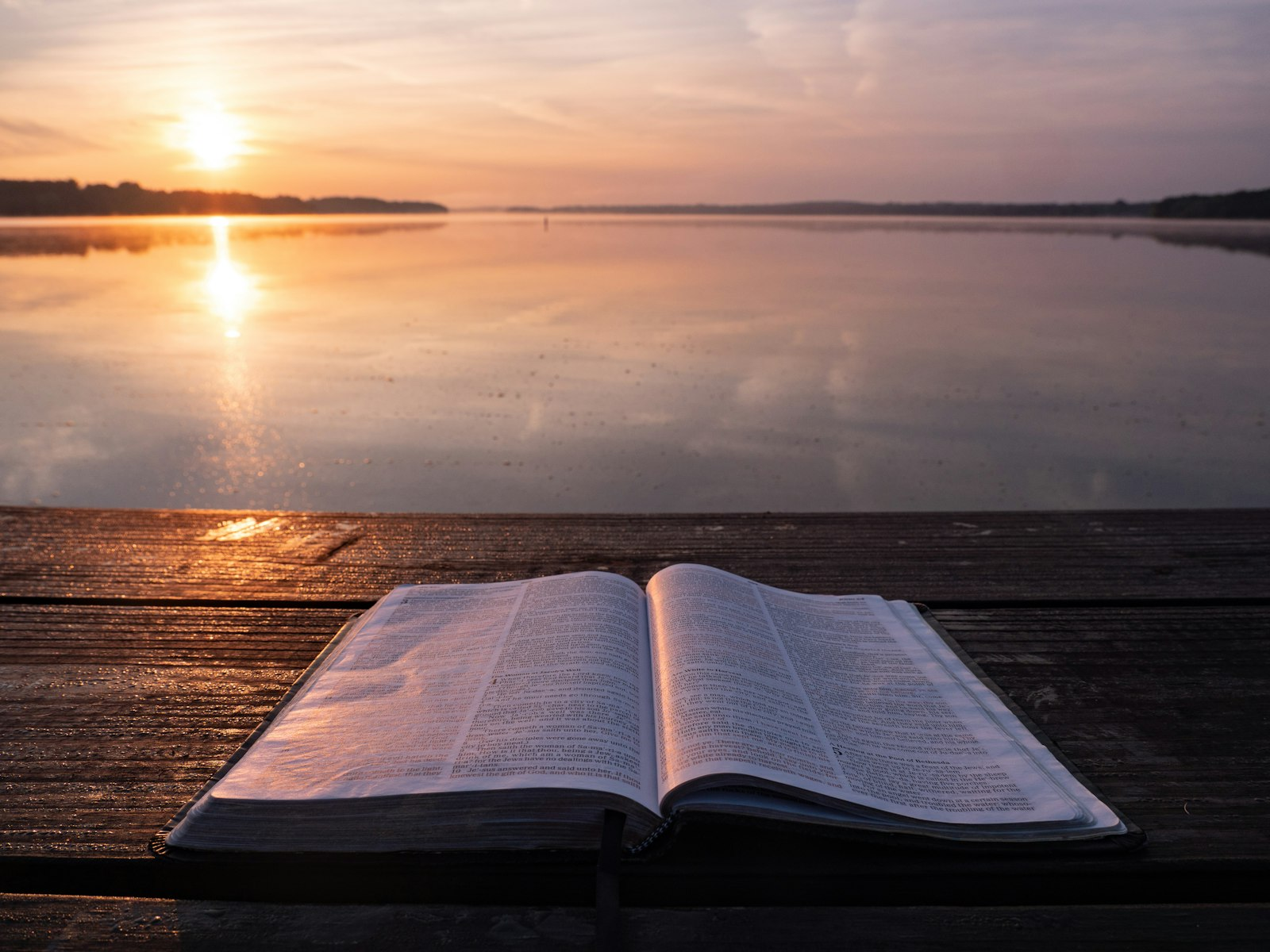 An open book on a table beside a lake in morning light, a quiet setting for learning how to hear God