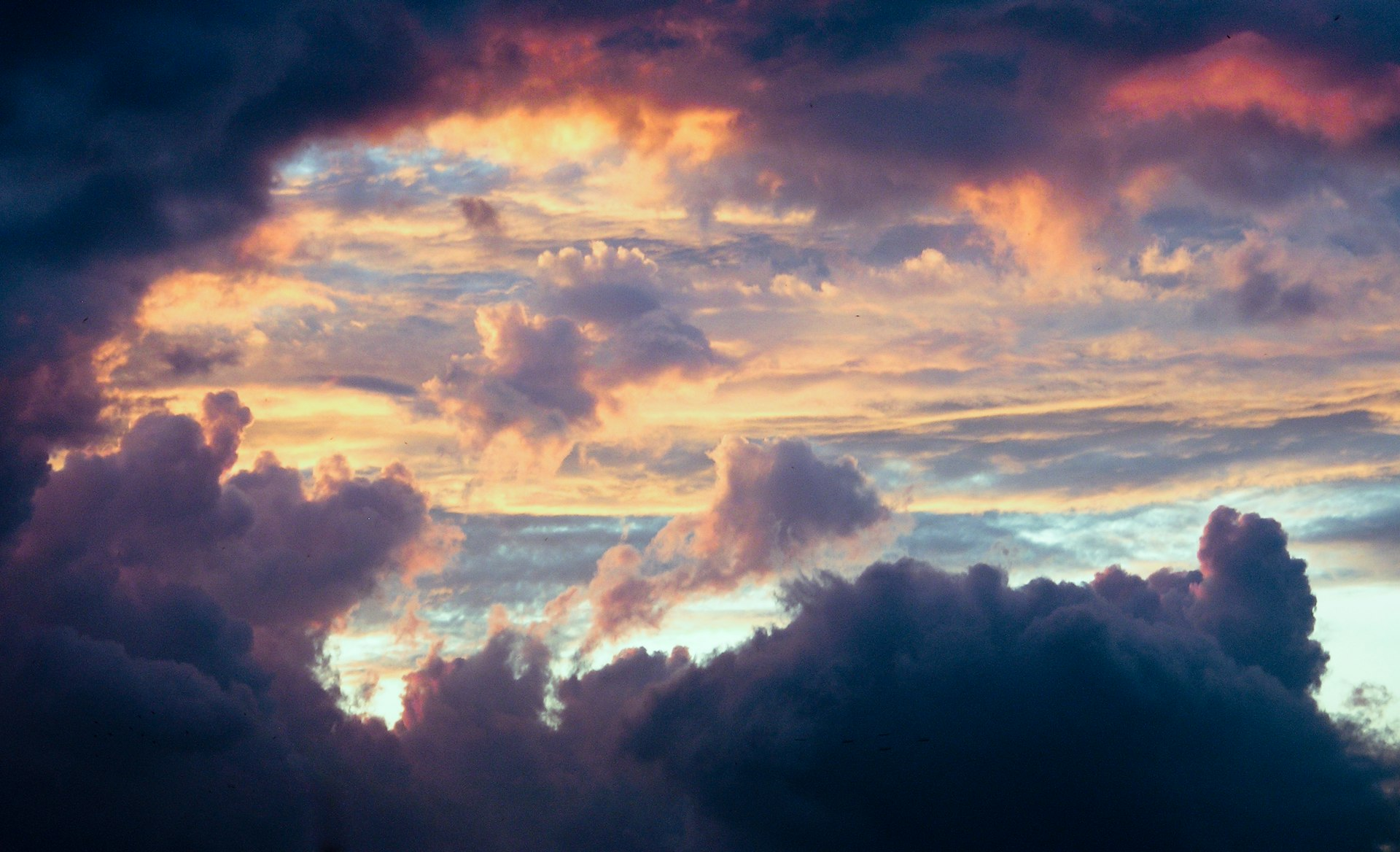 Dark storm clouds parting around a patch of warm golden light in the sky