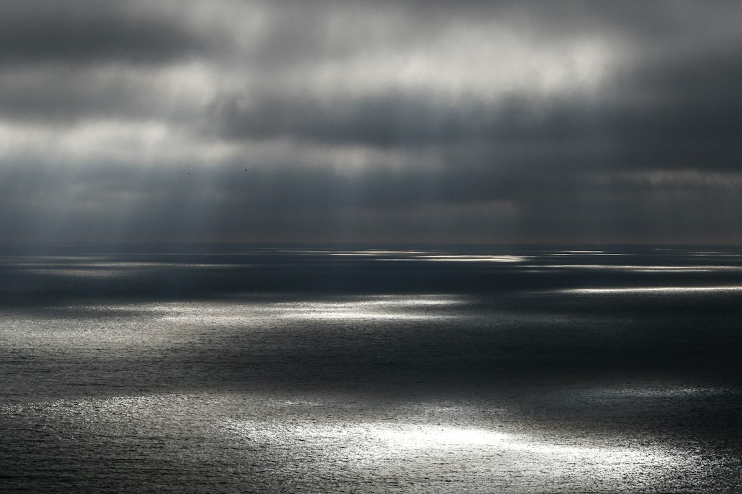 Shafts of sunlight breaking through dark storm clouds over the ocean